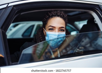 Young Business Woman Passenger Wearing A Medical Mask Looks Out Of A Taxi Car Window. Business Trips During Pandemic, New Normal And Coronavirus Travel Safety Concept.