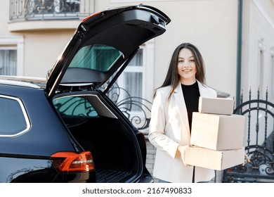 Young Business Woman Picking Up Parcels From A Car Trunk, Coming Home By Car