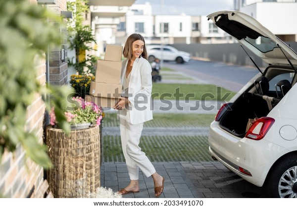 Young business woman picking up parcels from a car\
trunk, coming home by car. Concept of buying goods online and\
delivering them home