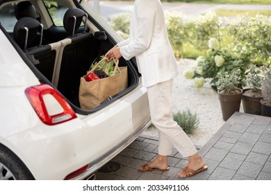 Young Business Woman Picking Up A Shopping Bag With Groceries From A Car Trunk, Shopping Healthy, Delivering And Wellbeing Concept