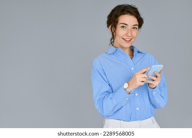 Young business woman professional manager worker holding mobile phone standing isolated at gray wall using cell phone for work, checking apps on cellphone, typing on smartphone tech device. - Powered by Shutterstock