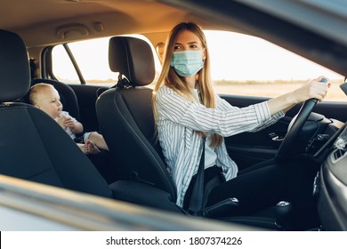 Young Business Woman In A Protective Medical Mask On Her Face, Driving A Car During A Trip With A Small Child In A Car Seat, Travel Concept