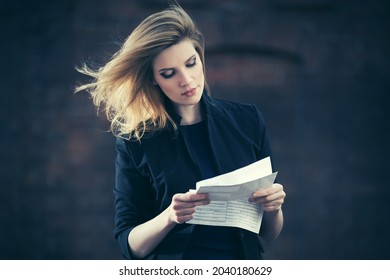 Young business woman reading tax letter on city street Stylish fashion model in black suit blazer