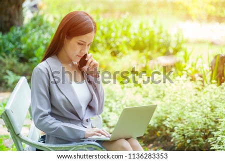 Young Business woman sitting on bench  talking on cell mobile phone and working with laptopcomputer in park.Morning light 
