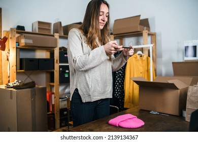 Young business woman takes a photo of a hat with her smartphone device to put it up for sale on a second-hand clothing platform - Millennial works online dresses store - New distance selling concept - Shutterstock ID 2139134367