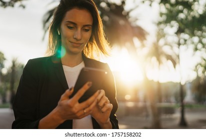 Young Business Woman Texting On Smartphone In City Park Barcelona Working In Sun Day, Happy Professional Girl Using  Mobile Gadget On Background Sun Flare Outdoors