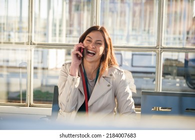 Young business woman waiting for the train sitting at the waiting room of train station - Cheerful and happy traveler talking on the smartphone while waiting for the train