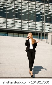 Young Business Woman Walk On Stairs Leaving Office Building And Talk On A Phone .