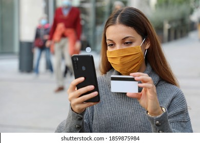 Young Business Woman Wearing Protective Mask With Credit Card And Smartphone Purchasing Outdoor. Successful Woman With Face Mask Is Using Mobile Phone And Bank Card For Online Shopping In City Street.