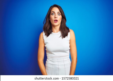 Young Business Woman Wearing White Elegant Dress Standing Over Blue Isolated Background Afraid And Shocked With Surprise Expression, Fear And Excited Face.