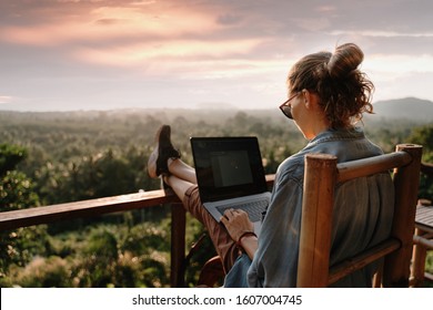 Young business woman working at the computer in cafe on the rock. Young girl downshifter working at a laptop at sunset or sunrise on the top of the mountain to the sea, working day.