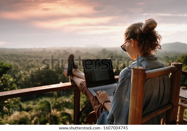 Young\
business woman working at the computer in cafe on the rock. Young\
girl downshifter working at a laptop at sunset or sunrise on the\
top of the mountain to the sea, working\
day.