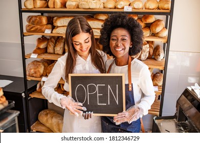 Young Business Women Holding An Open Sign. Bakery Shop Female Owner Showing Chalkboard With Open Sign While Opening Store. Local Business, Hospitality, Open After Lockdown Concept.