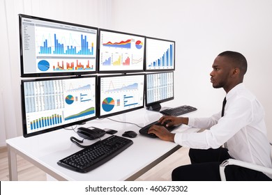 Young Businessman Analyzing Financial Chart On Multiple Computers In Office