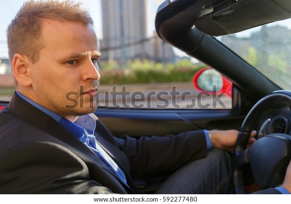 young businessman behind wheel driving luxury\
cabriolet, close-up