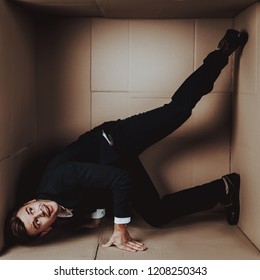 Young Businessman in Black Suit in Cardboard Box. Young Man in Suit. Life in Little Cardboard Box. Uncomfortable Life. Personal Spase Concept. Uncomfortable House Concept. Young Introvert.