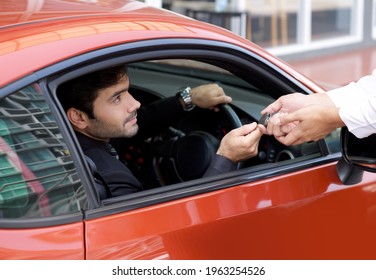 Young businessman in a black suit handling car key to the valet service staff while holding the car wheel.