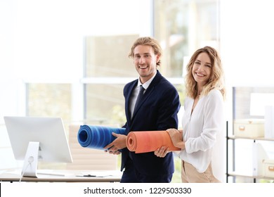 Young Businessman And Businesswoman Holding Yoga Mats In Office. Gym After Work