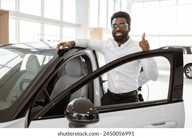 Young businessman buying automobile in light vehicles salon dealership store. Pensive African American man buyer in formal wear choosing new car in showroom with panoramic windows. Sales concept. - Powered by Shutterstock