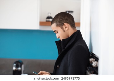 Young businessman checks his smartphone in a modern kitchen, embodying a professional yet relaxed lifestyle - Powered by Shutterstock