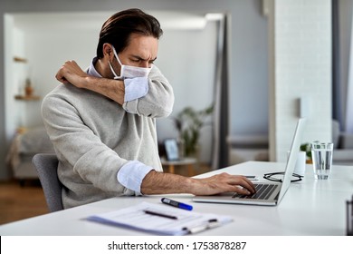 Young businessman coughing into elbow while wearing protective face mask and working on a computer at home.  - Powered by Shutterstock