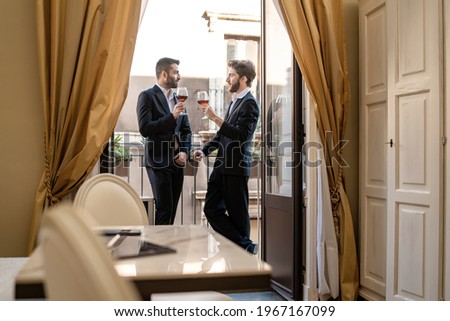 Young businessman discussing their business drinking red wine together in an hotel room balcony.