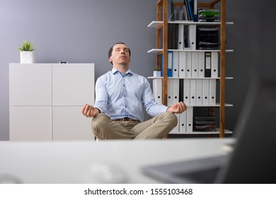 Young Businessman Doing Yoga Behind Desk In Office