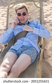 Young Businessman Downshifter Talking On The Phone While Lying On A Sun Lounger On The Beach Wearing A Shirt, Tie And Boxer Shorts. Vertical Shot