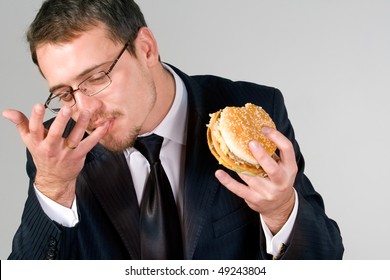 Young  Businessman Eating Hamburger, Licking Fingers