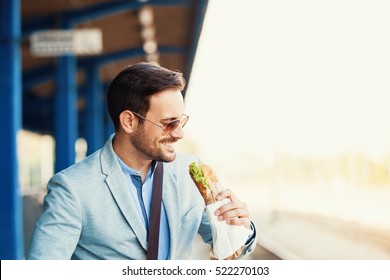 Young businessman is eating sandwich while waiting train.