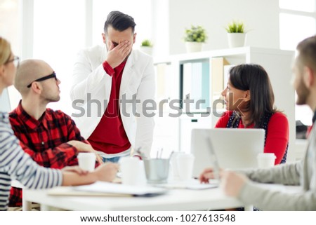 Young businessman expressing confusion in front of his colleagues during working meeting