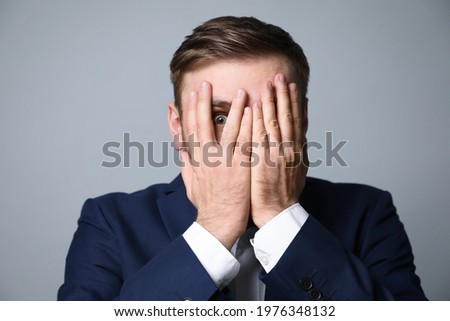Young businessman feeling fear on grey background