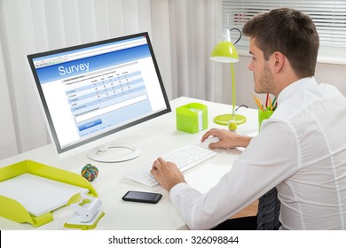 Young Businessman Filling Online Survey Form On Computer At Desk