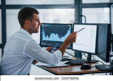 Young businessman in formal clothes is in office with multiple screens. Conception of exchange and money.
