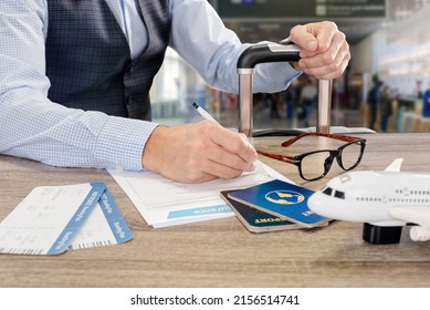 Young businessman with glasses, boarding pass and suitcase filling travel insurance form in airport