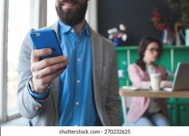 Young businessman in glasses with smartphone over woman working on laptop on background - Powered by Shutterstock