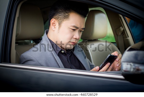 Young businessman in gray suit sitting in a\
new car and holding the mobile\
phone