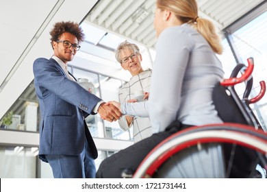 Young businessman greets colleague in wheelchair with handshake in the company