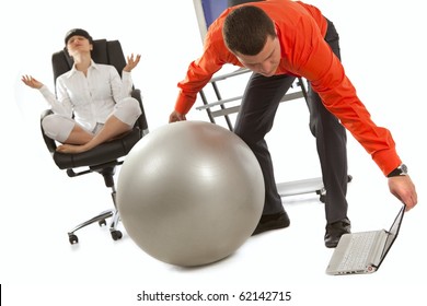 Young Businessman With Grey Ball, Looking On Laptop Screen. His Colleague, Doing Yoga On The Office Chair