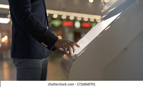 Young businessman hands dressed in jacket swiping for information in kiosk on background of lights of shopping mall. No face man with interactive wayfinding kiosk