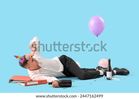Young businessman with hangover after Birthday party lying on blue background