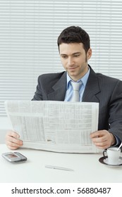 Young Businessman Having Coffee Break, Sitting At Office Desk And Reading Newspaper.