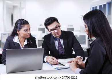 Young businessman with his assistant showing and explaining a business document to their partner