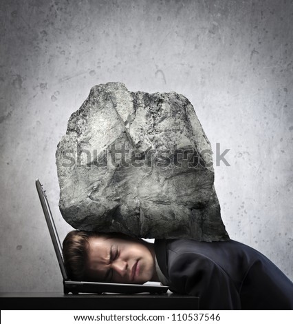Young businessman with his head squeezed between a laptop keyboard and a rock