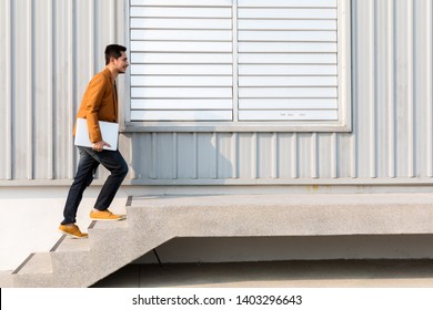 Young businessman holding laptop walking up the stairs with success, copy space
