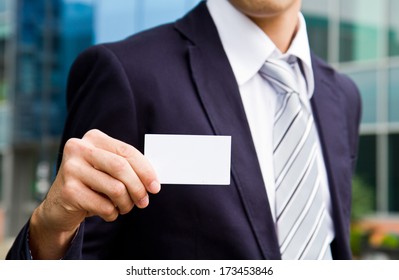 Young Businessman Holding Visit Card In Hand And Standing In The Front Of Office Building 