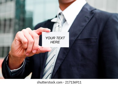 Young Businessman Holding Visit Card In Hand And Standing In The Front Of Office Building 