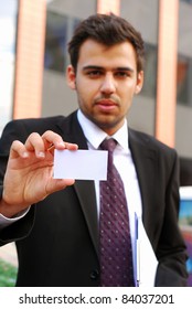 Young Businessman Holding Visit Card In Hand And Standing In The Front Of Office Building