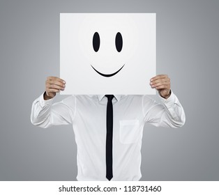 Young Businessman Holding White Card With A Happy Face On It Isolated On Gray Background