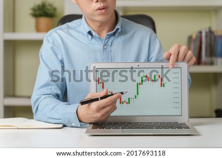 Young businessman or investor pointing on stock tickers or Cryptocurrency trading graphs to teach about investing new stock trading, Cryptocurrency as Bitcoin platform at home. Young investor concept